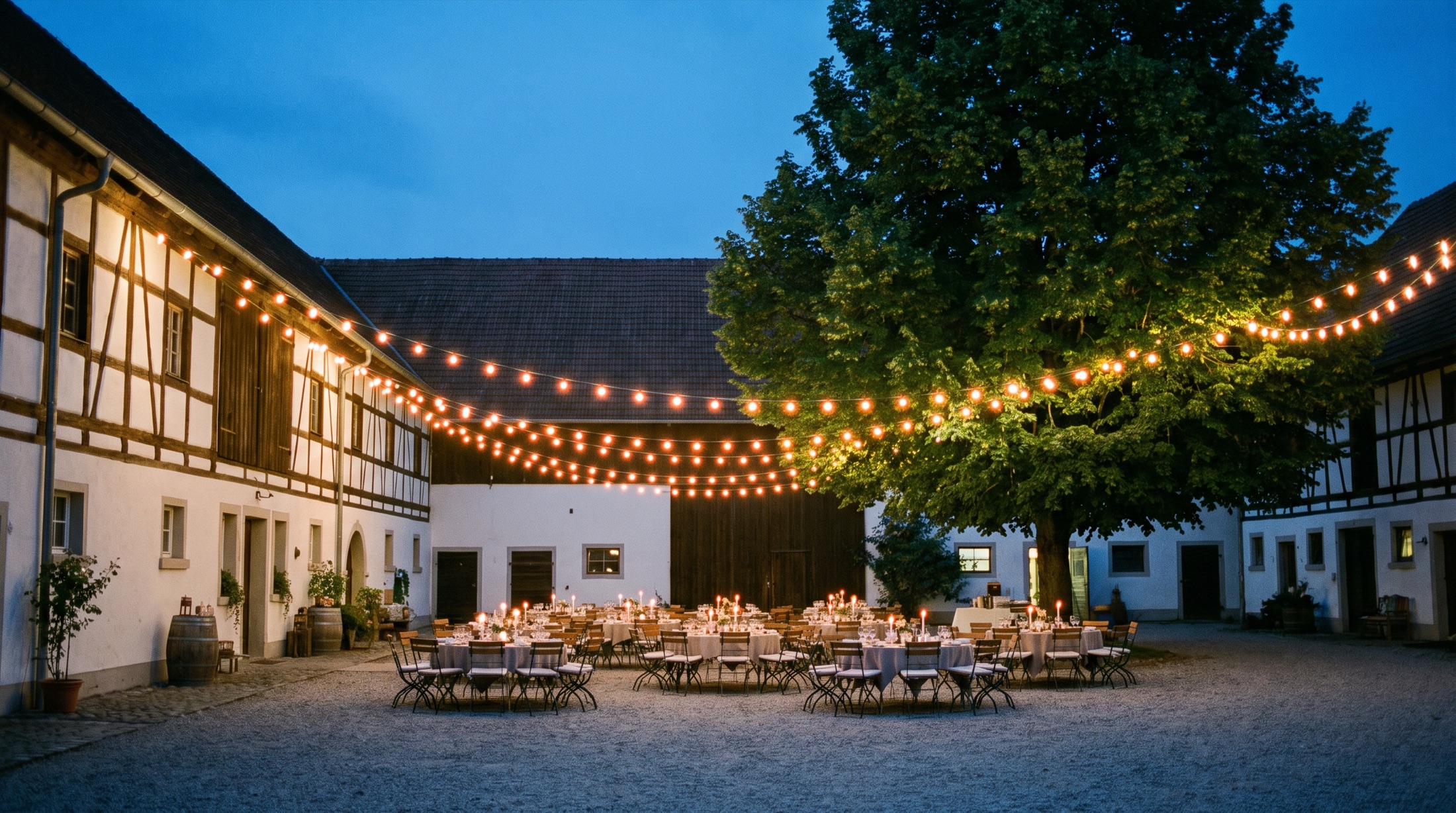 Der Innenhof zur blauen Stunde: Lichterketten über runden Tischen mit Kerzen, Fachwerk ringsum